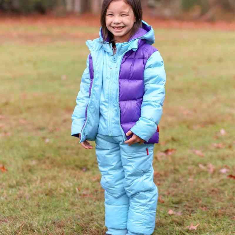 Child standing outdoors in One Kid Packable Snow Pant in Aqua wearing matching Road Coat.