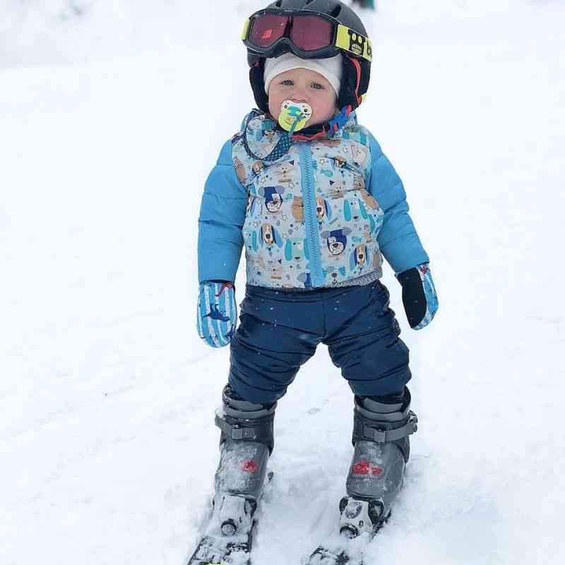 Child wearing navy Packable Snow Pants and a light blue Road Coat, playing in the snow, highlighting warmth and comfort.