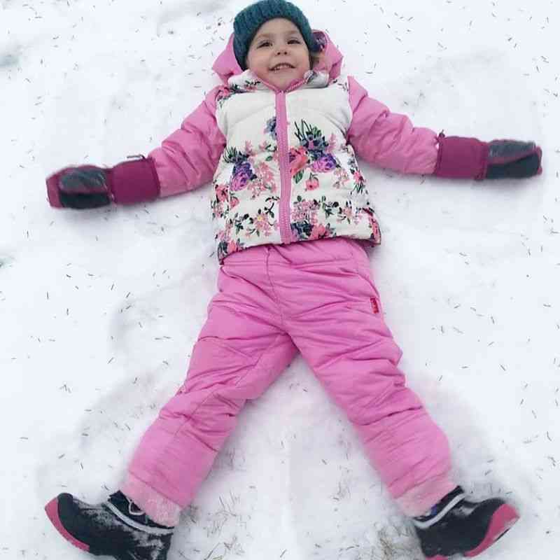 Child making a snow angel wearing One Kid Packable Snow Pant in pink with matching Road Coar.