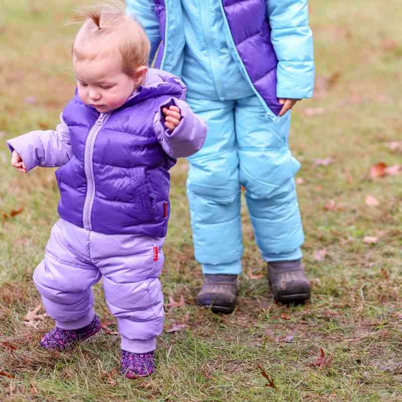 Two children playing outdoors in One Kid Packable Snow Pants, Violet and Aqua wearing matching Road Coats.