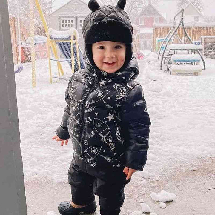 Little Boy wearing the One Kid Quilted Bomber hat in black with matching Road Coat and soft pack-able snow pant.