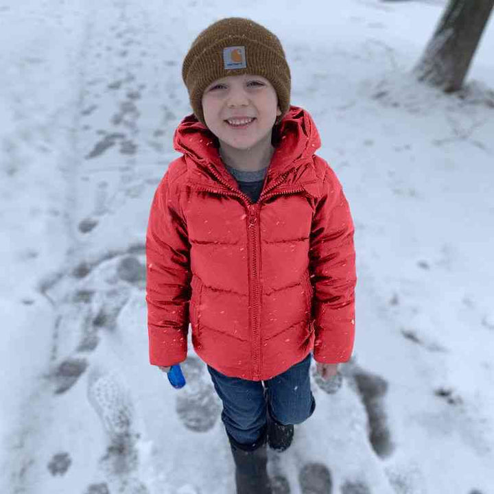 Child wearing the red Road Coat, smiling while standing on a snowy path, highlighting the coat’s comfort and cold-weather suitability.